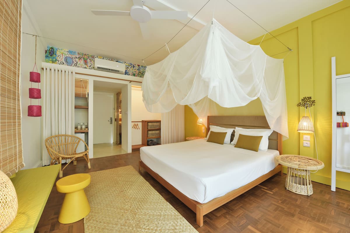 A bedroom with a bed, a bedside table, a chair, a ceiling fan, and a window with blinds.