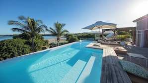 A swimming pool with a view of the sea, surrounded by palm trees and lounge chairs. - Veranda Tamarin Hotel & Spa (Tamarin)