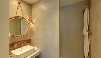 Un baño con un espejo redondo, un lavabo y una zona de ducha.