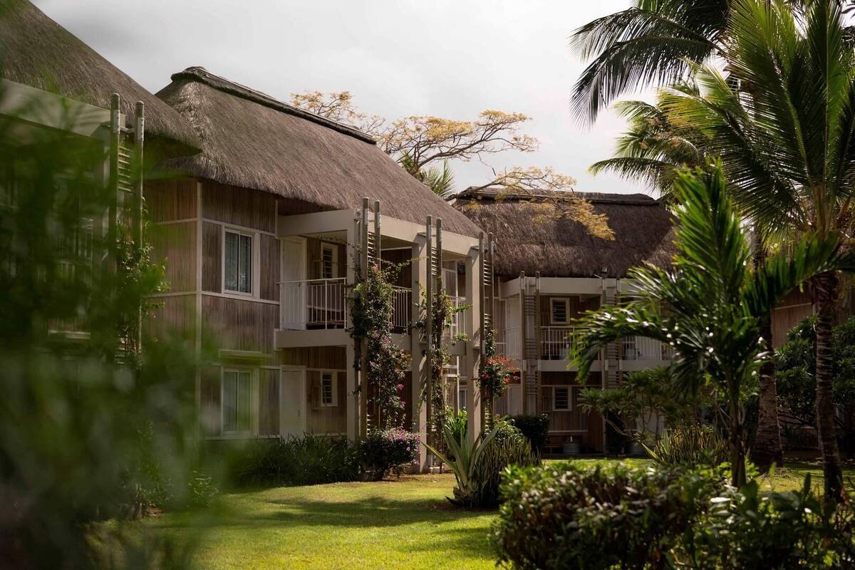 A resort with thatched-roof buildings, a well-maintained garden, and a clear sky.