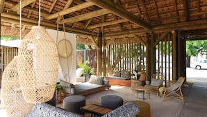 A covered outdoor seating area with a thatched roof, wicker furniture, and a hanging light fixture. - Veranda Tamarin Hotel & Spa (Tamarin)