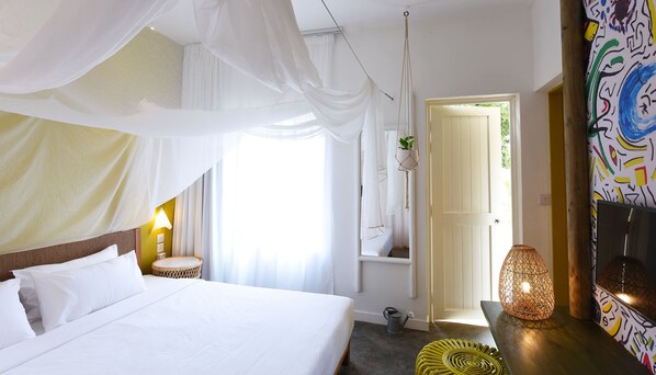 A bedroom with a bed, a bedside lamp, a hanging plant, and a door leading to another room.