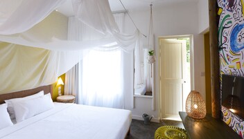 Un dormitorio con cama, lámpara de noche, planta colgante y puerta que da a otra habitación.