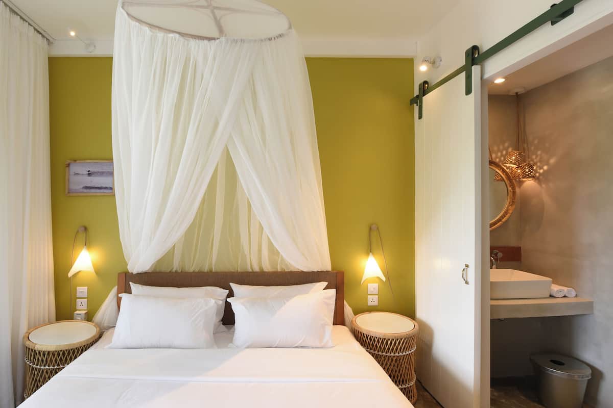 A bed with a canopy, two bedside lamps, a wicker side table, and a wall-mounted mirror.