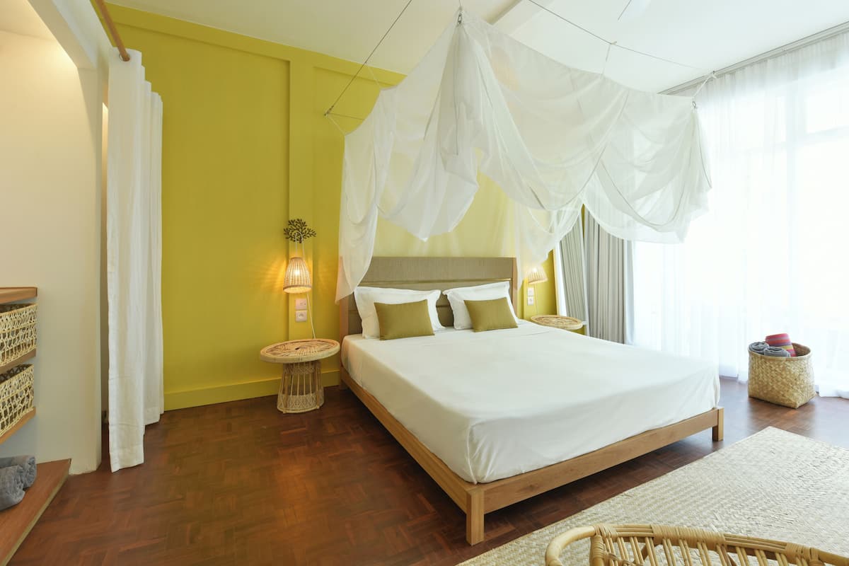 A bedroom with a bed, bedside tables, a canopy, and a wicker chair.
