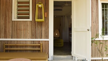 Fachada de madera con un banco, una puerta y una ventana con persianas.