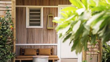 A wooden wall with a window and a hanging lantern, a wooden bench with cushions, and a metal barrel.