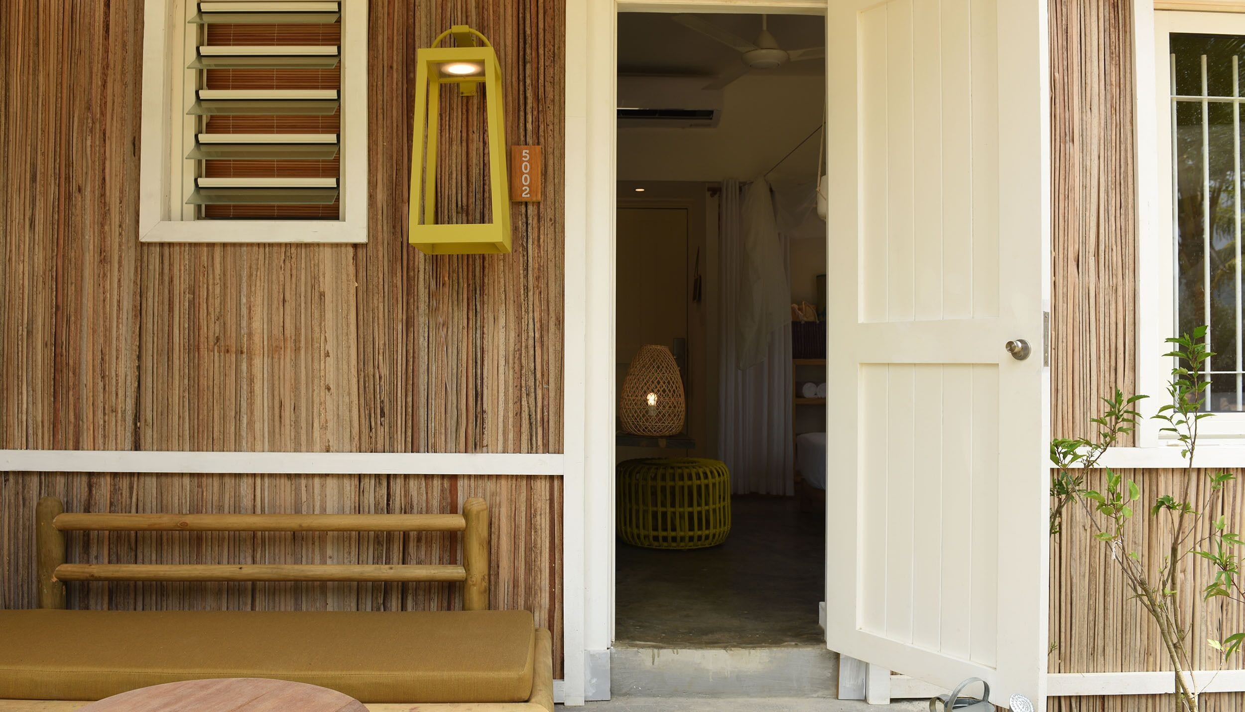 A wooden exterior with a bench, a door, and a window with blinds.