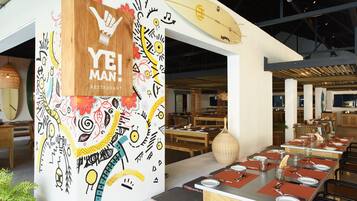 A restaurant interior with a wooden sign reading 'YE! MAN! RESTAURANT', tables set with plates and cutlery, and a surfboard decoration on the wall.