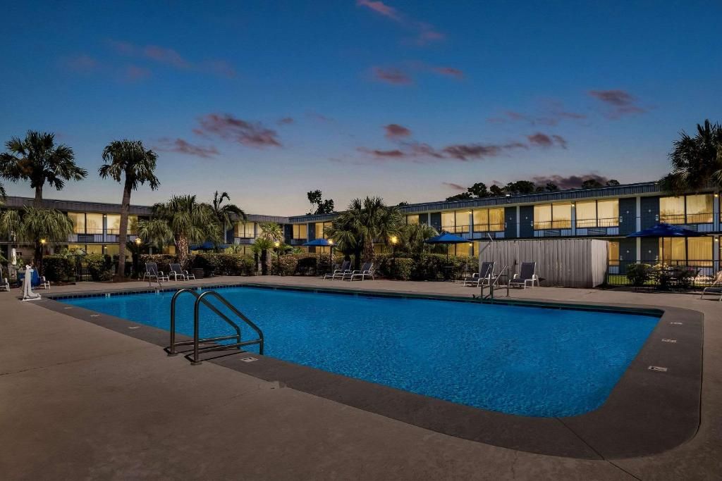 A hotel with a swimming pool, palm trees, and a building with multiple windows.