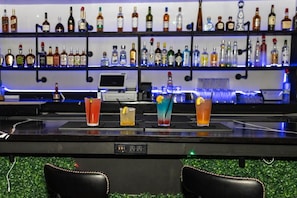 A bar area with a variety of liquor bottles on shelves, a digital screen, and several glasses of mixed drinks on the counter. - Suburban Studios Slidell I-10 (Slidell)
