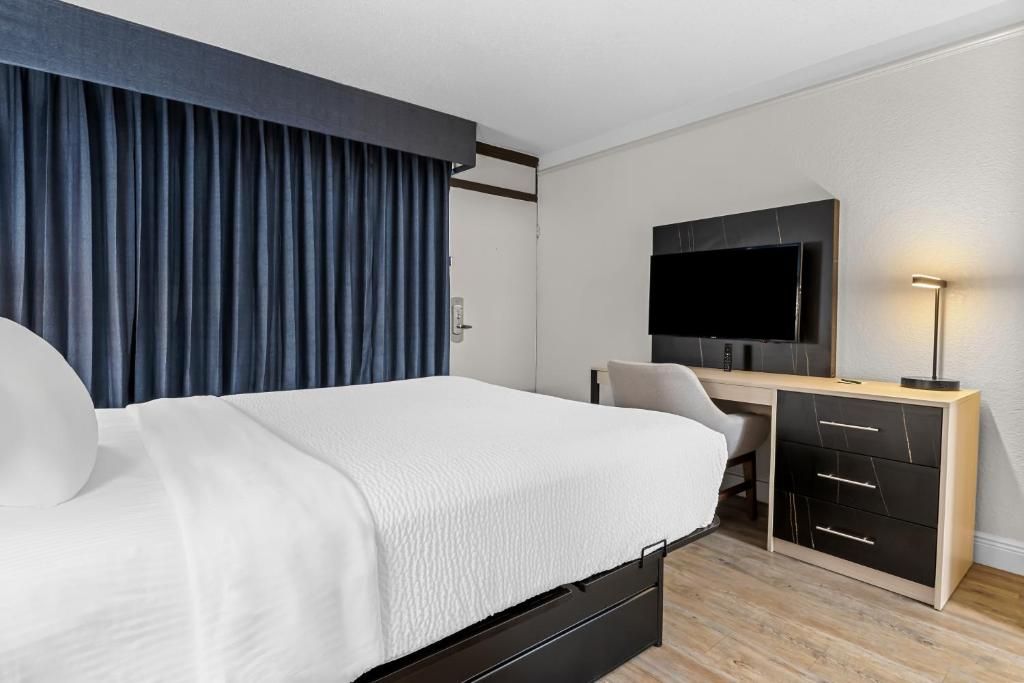 A hotel room with a bed, a desk, a chair, a television, and a desk with drawers.