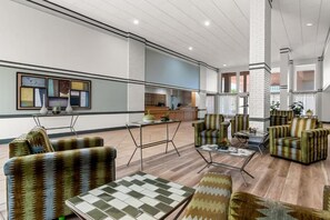 Eine großzügige Lobby mit einer Rezeption, einer Sitzecke mit gemusterten Sofas und einer modernen Küche im Hintergrund.