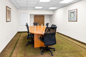 Un salón de conferencias con una mesa redonda, sillas negras, una pizarra y obras de arte enmarcadas en las paredes.