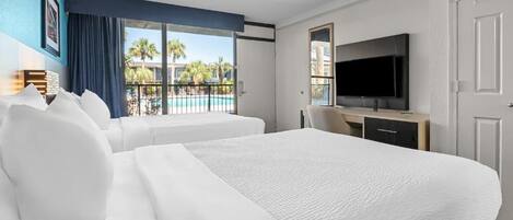 Habitación de hotel con dos camas, televisión, escritorio y vista a una piscina.