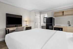Een hotelkamer met een groot bed, een bureau met stoel, een televisie, een koelkast, een wastafel en een spiegel.