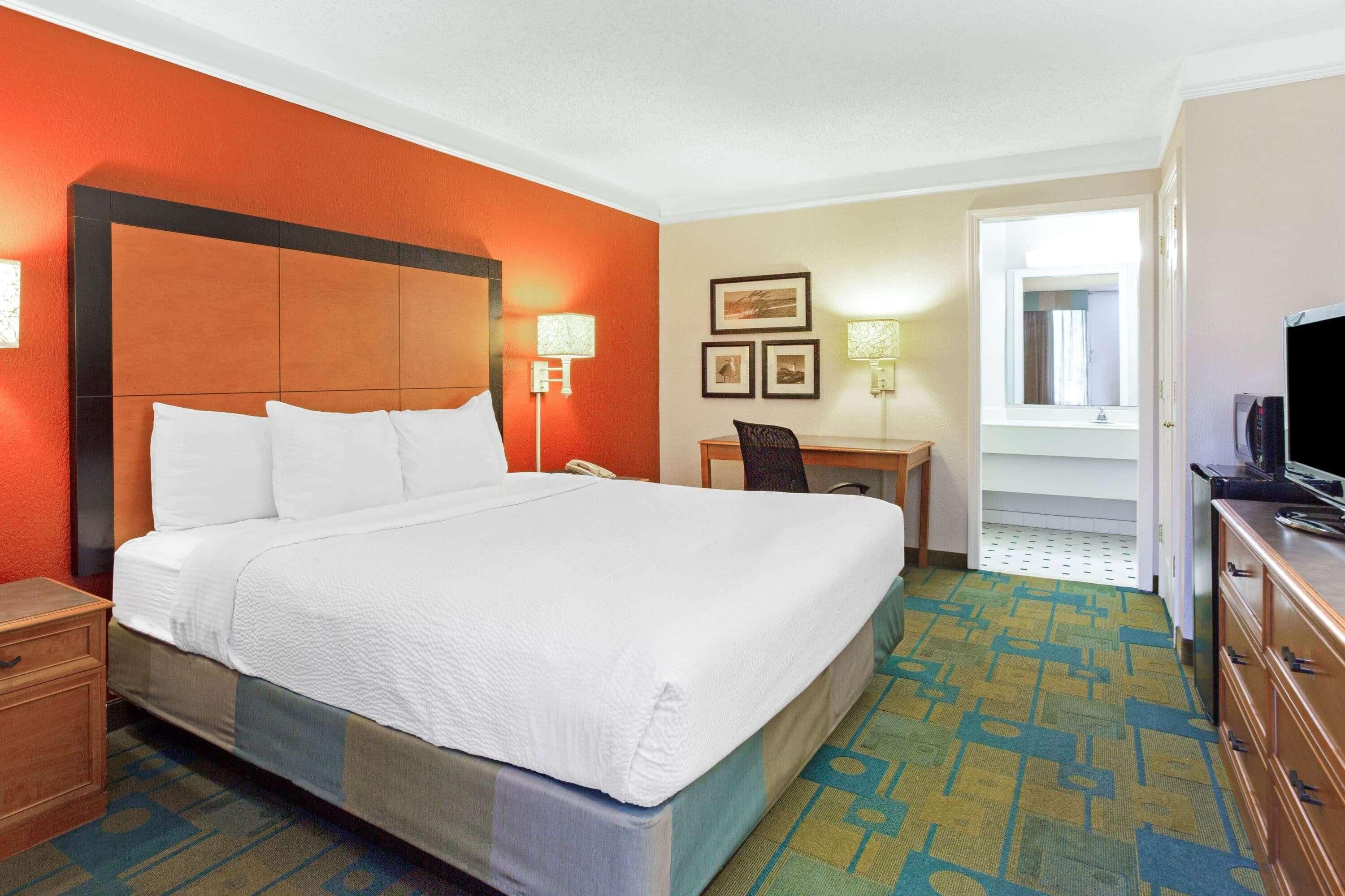 A hotel room with a large bed, a desk, a chair, a television, and a window.