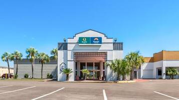 A hotel with a clear entrance, a parking lot, and palm trees in the vicinity.