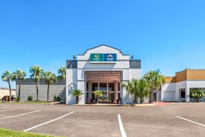 Un hotel con entrada despejada, estacionamiento y palmeras cercanas.