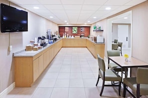 A modern kitchen with a flat-screen TV, wooden cabinets, a central island, and a dining area with chairs. - Rodeway Inn Slidell I-10 (Slidell)
