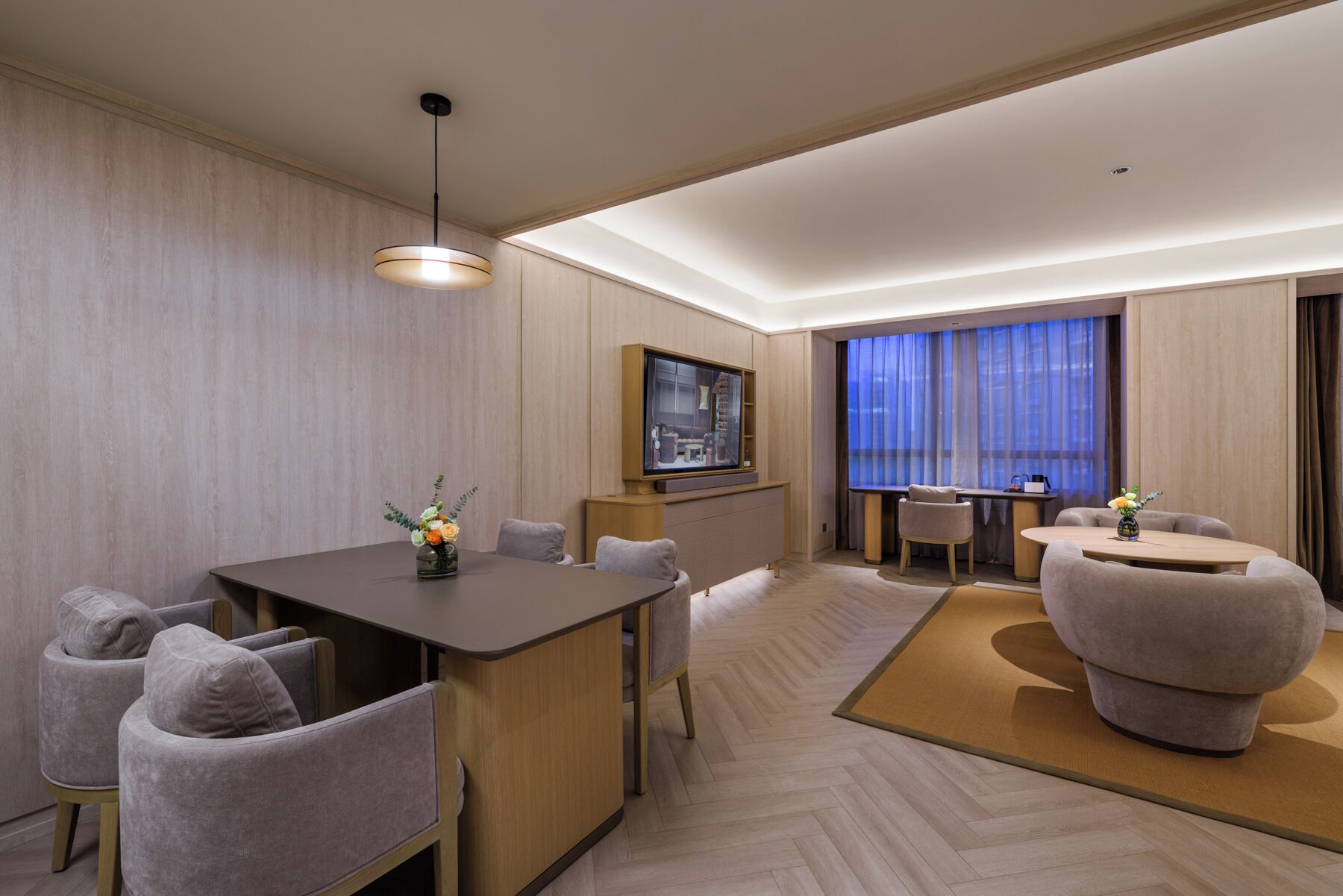 Habitación de hotel con comedor, televisor y zona de estar con vistas a la ciudad.