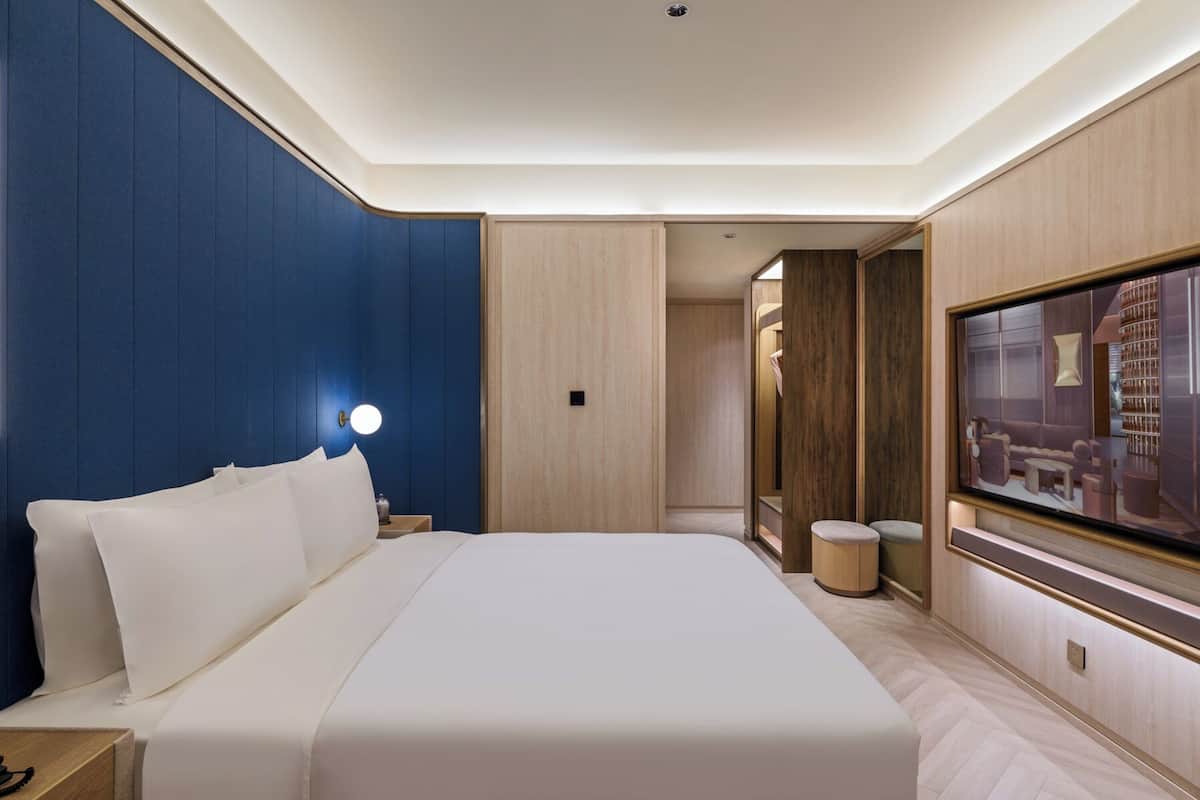 Una habitación de hotel con una cama grande, televisión, mesita de noche y espejo.