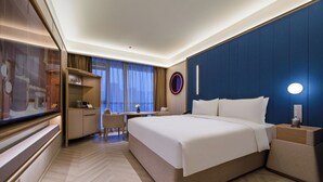 Habitación de hotel con cama, mesita de noche, escritorio, silla y un ventanal con cortinas.