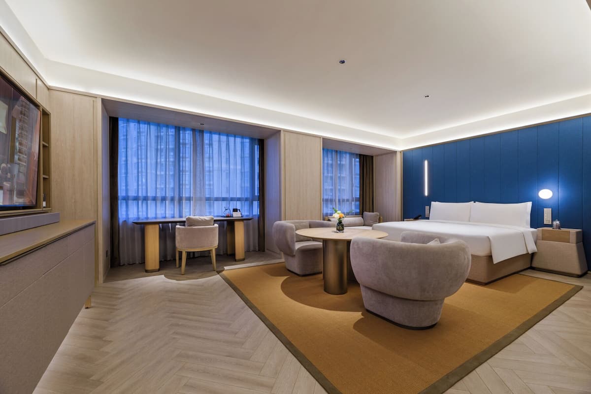 Una habitación de hotel moderna con cama, zona de estar y ventanas amplias.