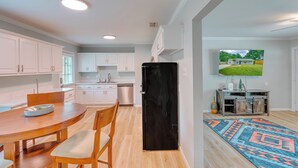 Cocina moderna con armarios blancos, un refrigerador negro y un comedor con mesa y sillas de madera.