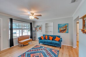 A modern living room with a blue sofa, a wooden floor, a ceiling fan, and artwork on the walls.