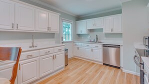 Una cocina moderna con armarios blancos, lavavajillas de acero inoxidable y una mesa de comedor de madera.