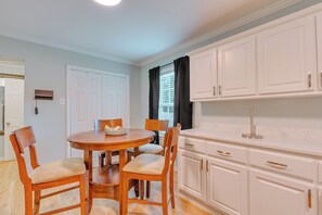 A dining area with a round wooden table, four chairs, and a window with black curtains. - Dog River Waterfront Retreat w/ Dock, Boat Lift & Gulf Access (Mobile)