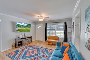 A living room with a television, a ceiling fan, a sofa, a chair, and a large window. - Dog River Waterfront Retreat w/ Dock, Boat Lift & Gulf Access (Mobile)