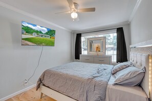 A bedroom with a bed, a ceiling fan, a TV mounted on the wall, a dresser, and a window with curtains. - Dog River Waterfront Retreat w/ Dock, Boat Lift & Gulf Access (Mobile)