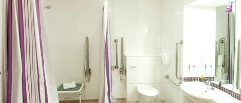 Un baño con ducha, inodoro y lavamanos, equipado con barras de apoyo y un secador de manos.
