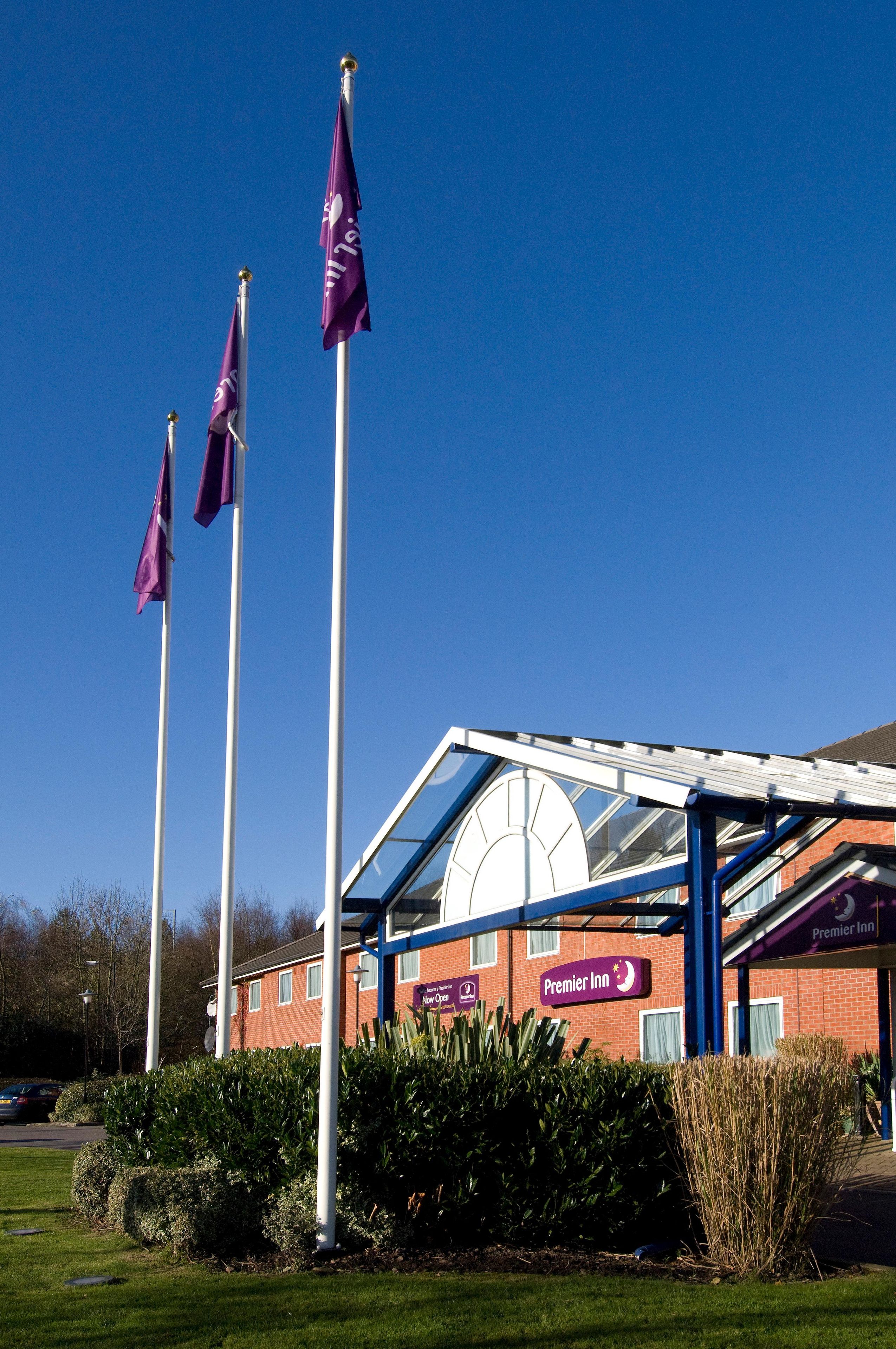 A hotel with a glass facade, a sign for Premier Inn, and three flags.