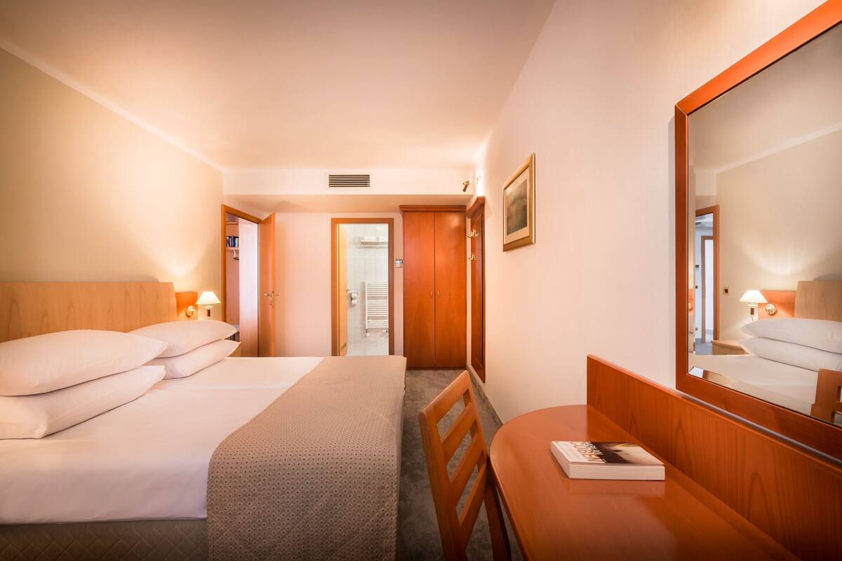 Habitación de hotel con cama, escritorio, silla, espejo y puerta que da a otra habitación.