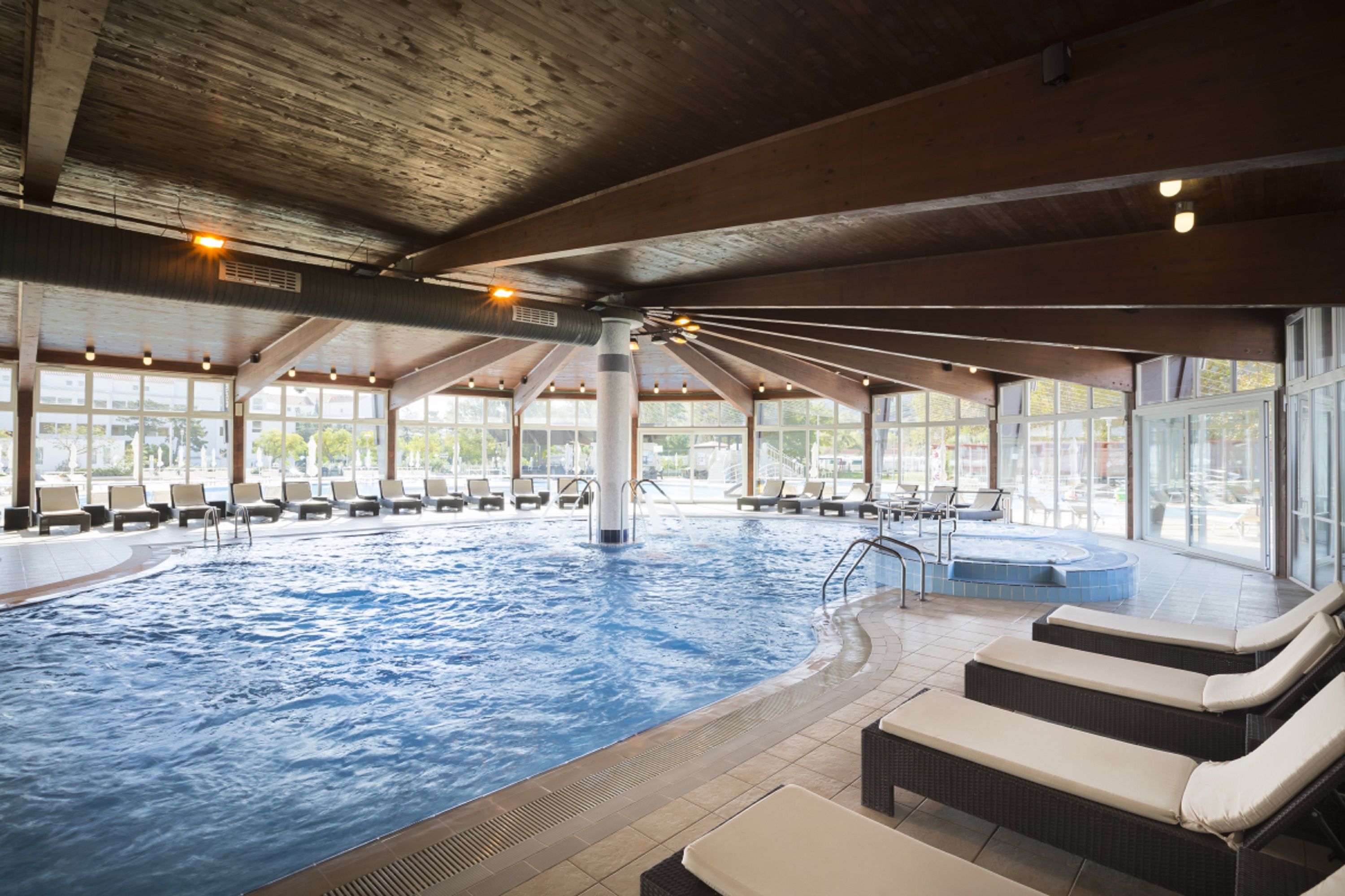 En inomhuspool med solstolar, ett bubbelbad och stora fönster.