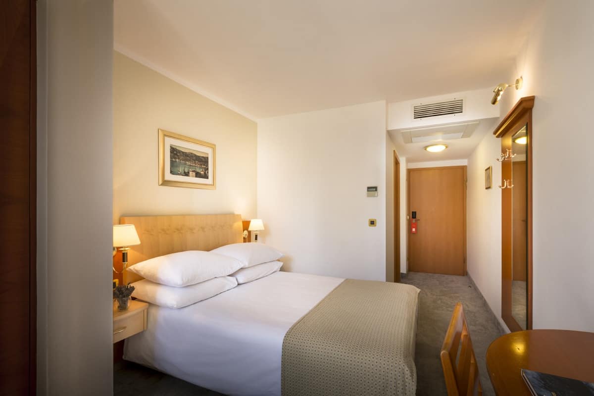 Una habitación de hotel con cama, mesita de noche, lámpara y un cuadro en la pared.