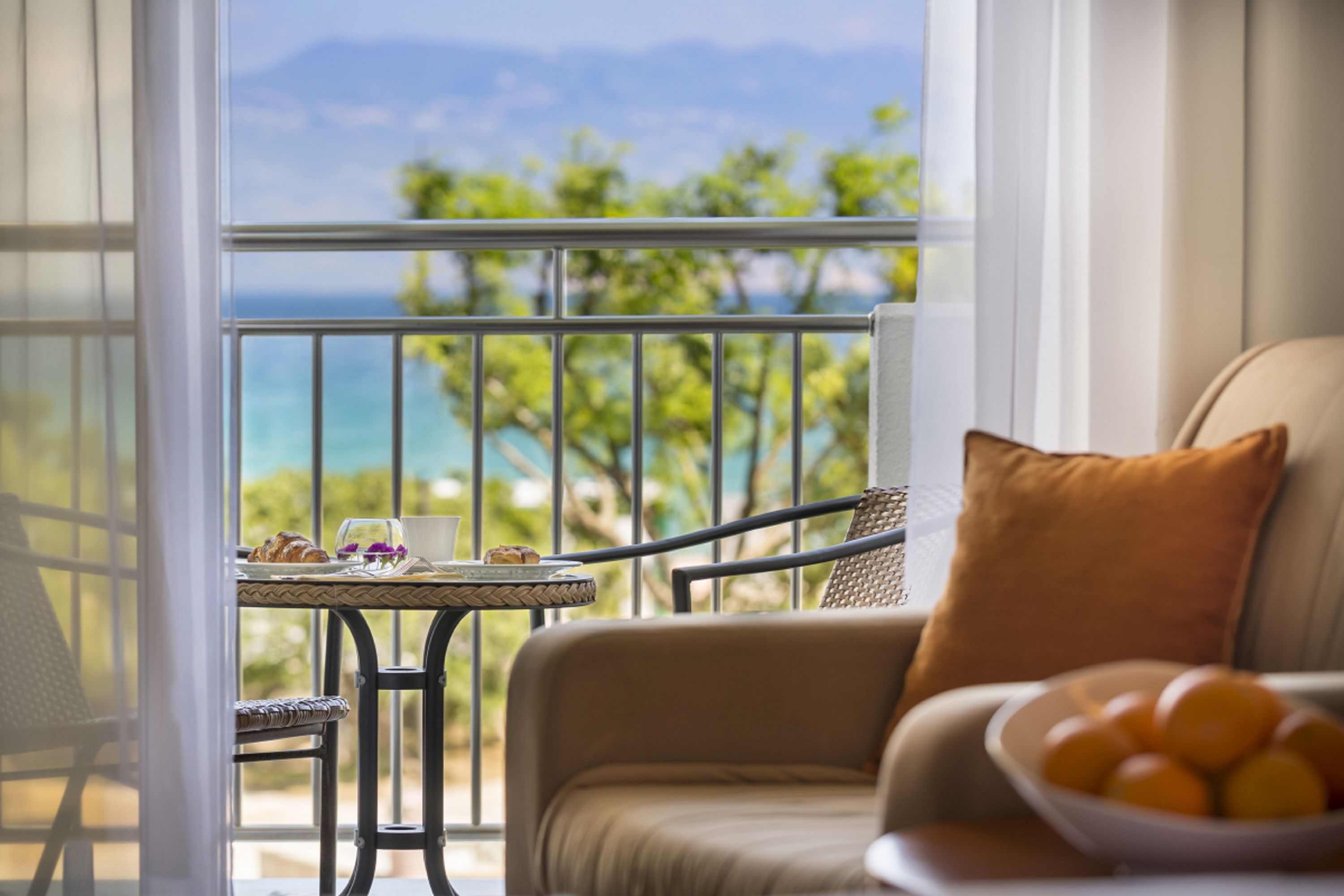 A balcony with a table, a chair, and a sofa with a bowl of fruit.