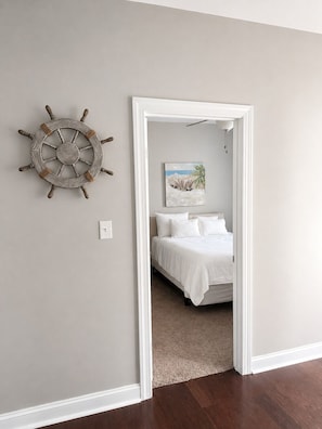 Ein Schlafzimmer mit einem Bett, einem an der Wand befestigten Steuerrad und einem Gemälde einer Strandansicht.