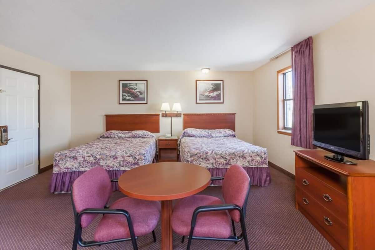 Quarto de hotel com duas camas, televisão, mesa com cadeiras e cômoda.