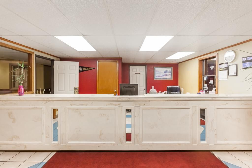 Un comptoir d’accueil avec un mur rouge, une horloge et des tableaux encadrés.