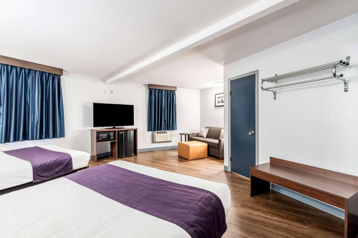 A hotel room with two beds, a TV, a desk, a chair, a bench, and a coat rack.