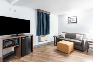 Sala de estar con televisor de pantalla plana, microondas integrado, mini refrigerador, sofá gris y una mesa de centro de madera.