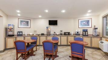 Une chambre d’hôtel équipée d’une kitchenette, d’un téléviseur à écran plat, d’œuvres d’art encadrées et d’un coin salon avec des fauteuils.