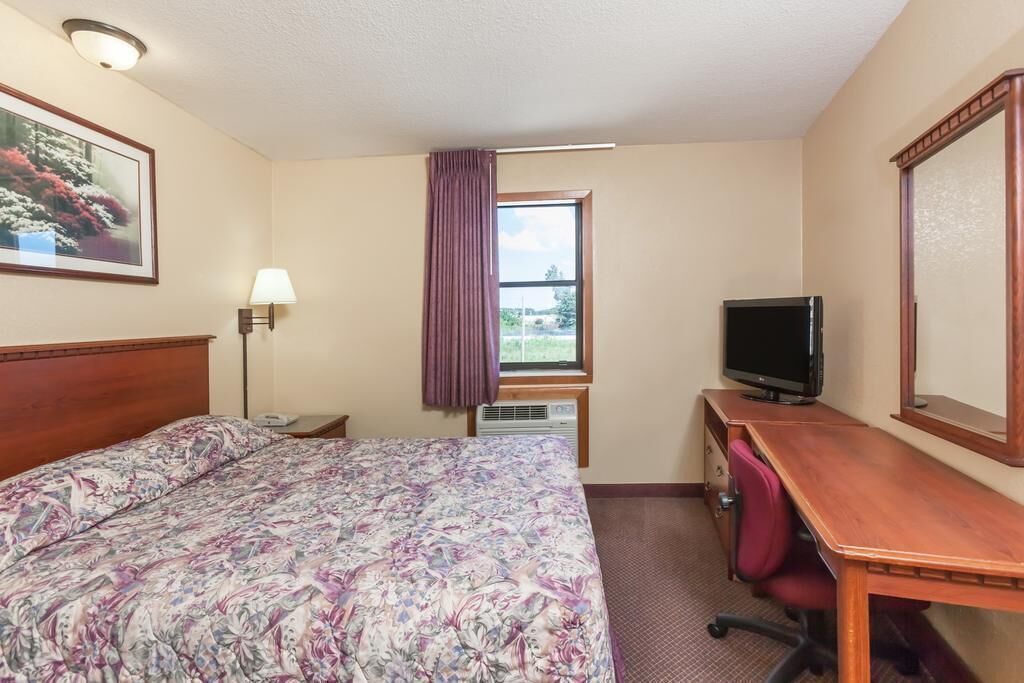 A hotel room with a bed, a desk, a television, a lamp, and a window with a view of greenery.