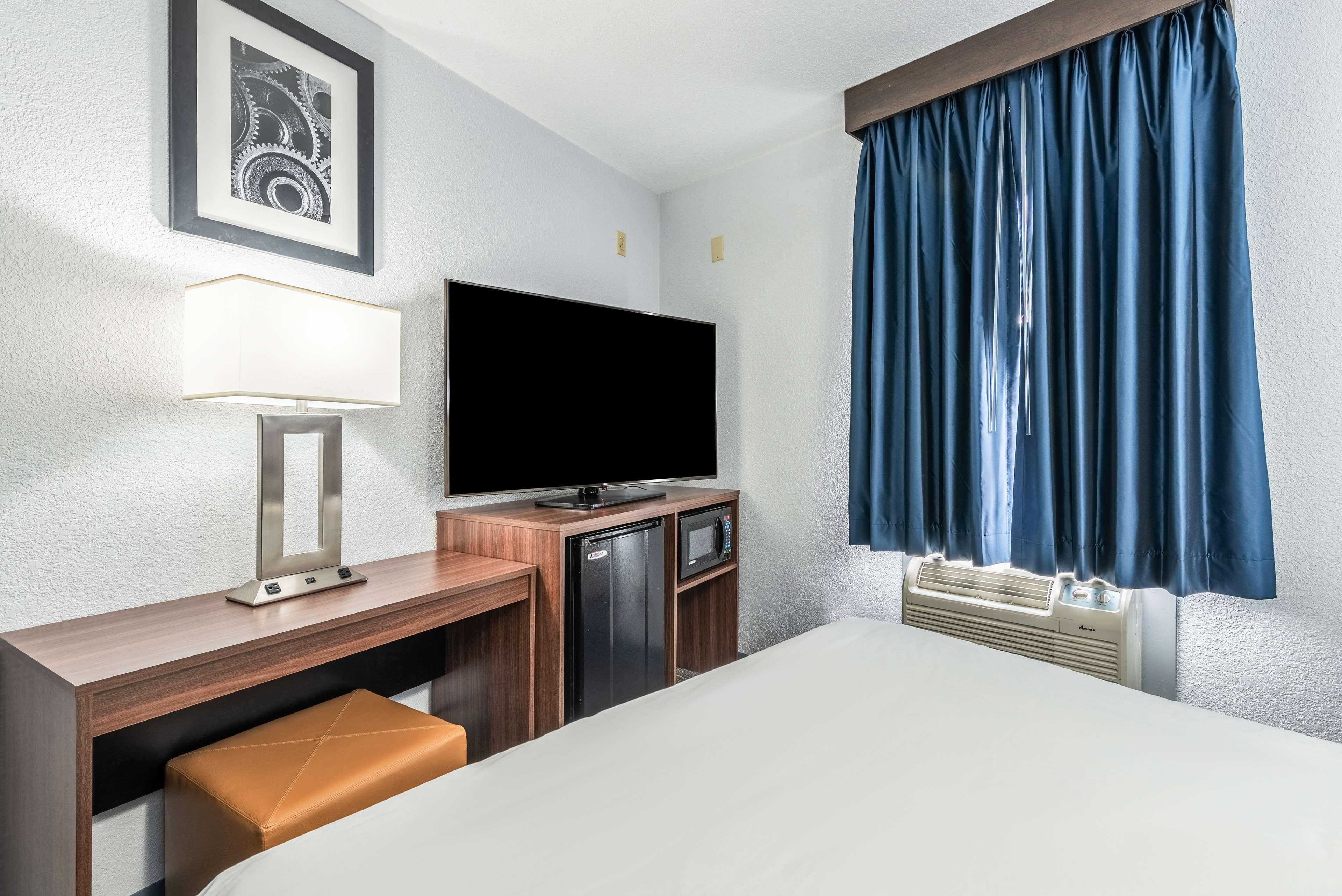 A hotel room with a bed, a desk with a lamp, a television, a microwave, and a window with curtains.