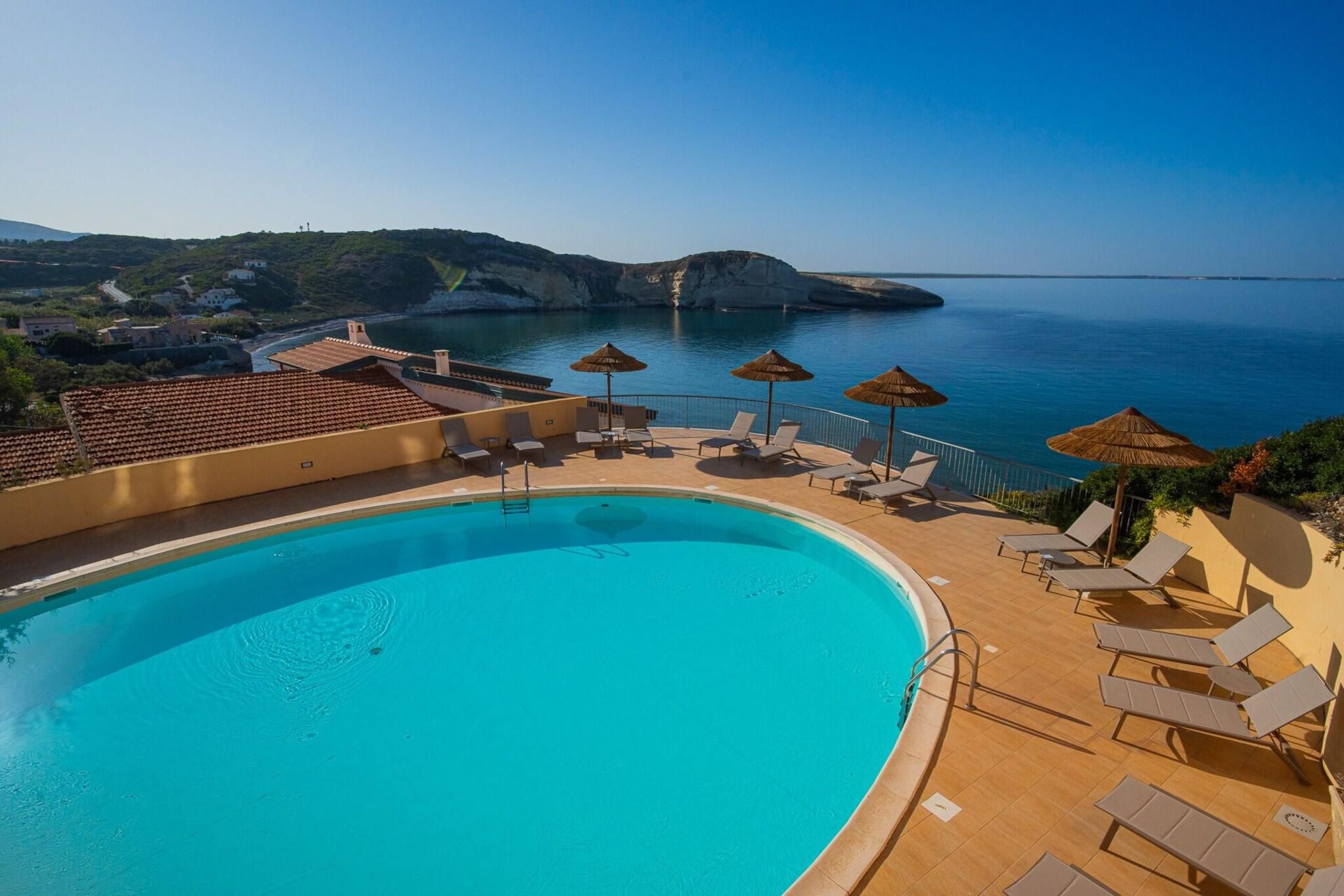 Ein Pool mit Liegestühlen und Sonnenschirmen mit Blick auf eine Küstenlandschaft mit Gebäuden und Klippen.