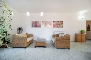 A room with wicker furniture, a tiled floor, and wall-mounted artwork. - Hotel la Baja (Cuglieri)